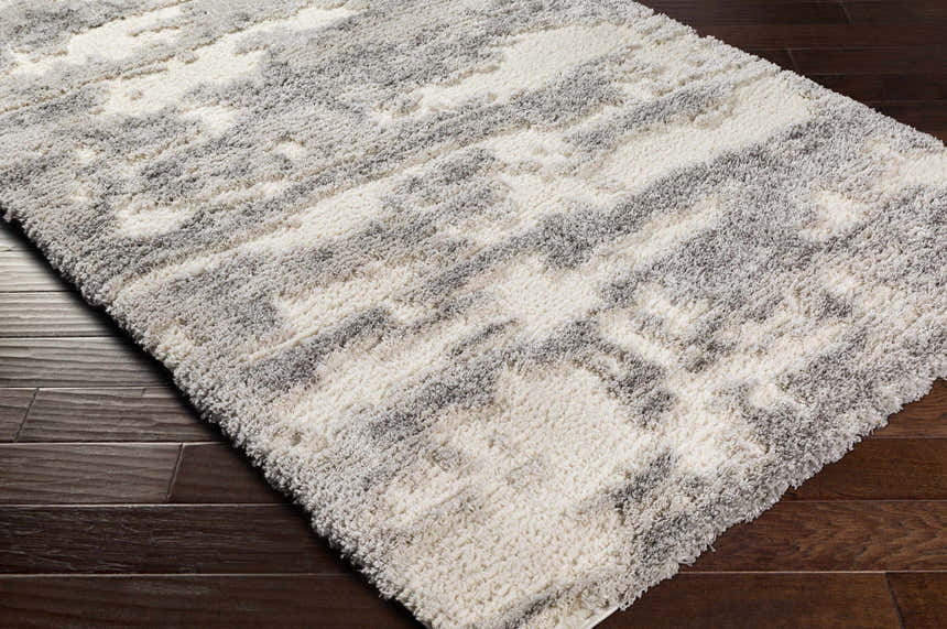 Close-up of the Dagami Area Rug. Gray and white shag rug with a contemporary pattern and soft, textured pile. Corner