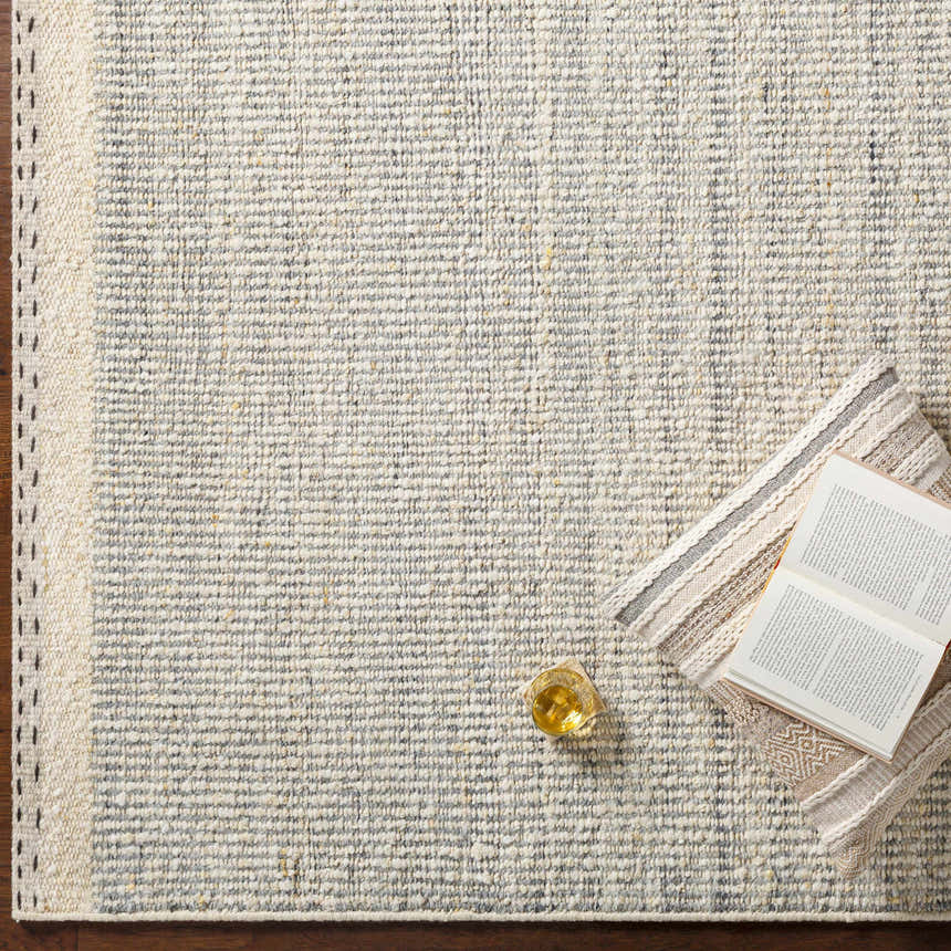 Close-up of the Dalaoig Flat Woven Wool Rug in cream and gray. Hand-woven texture with a book and drink for a cozy feel. Styleshot