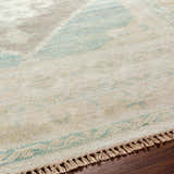 Close-up of the hand-knotted Danao Premium Rug. Cream wool rug with dusty pink, ice blue, and light gray accents. Tassel fringe detail. Texture