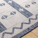 Close-up of the Dapitan Indoor & Outdoor Rug. Features a geometric pattern in denim blue on a light gray, woven texture. Texture
