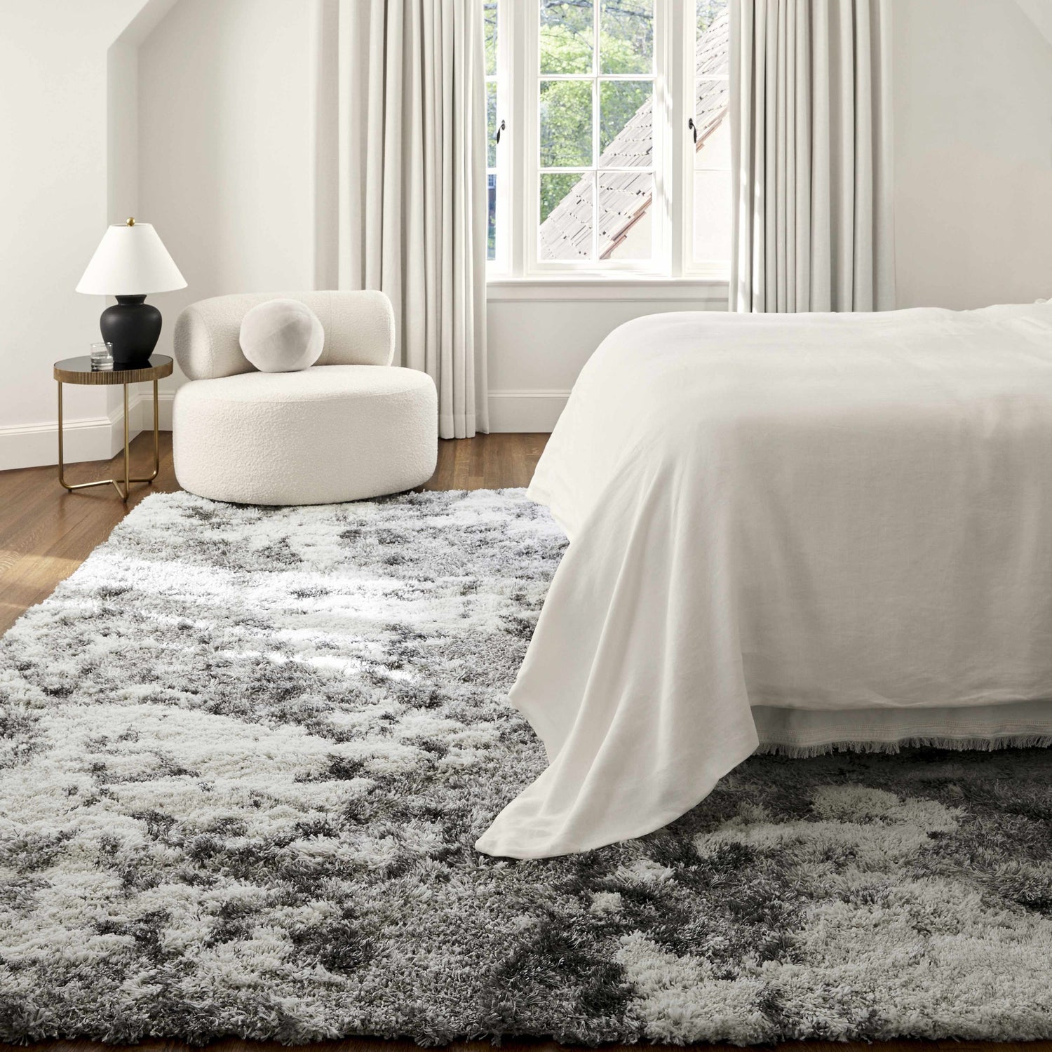Bedroom scene with a gray and white Dawesville shag rug, white bed linens, and a modern white chair near a window. Roomscene-Rectangle