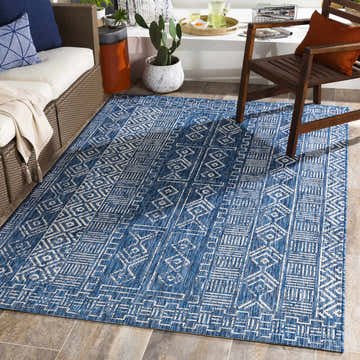 Outdoor patio scene with blue and white geometric Deeth Area Rug, wicker sofa, and wooden chair. Roomscene-Rectangle