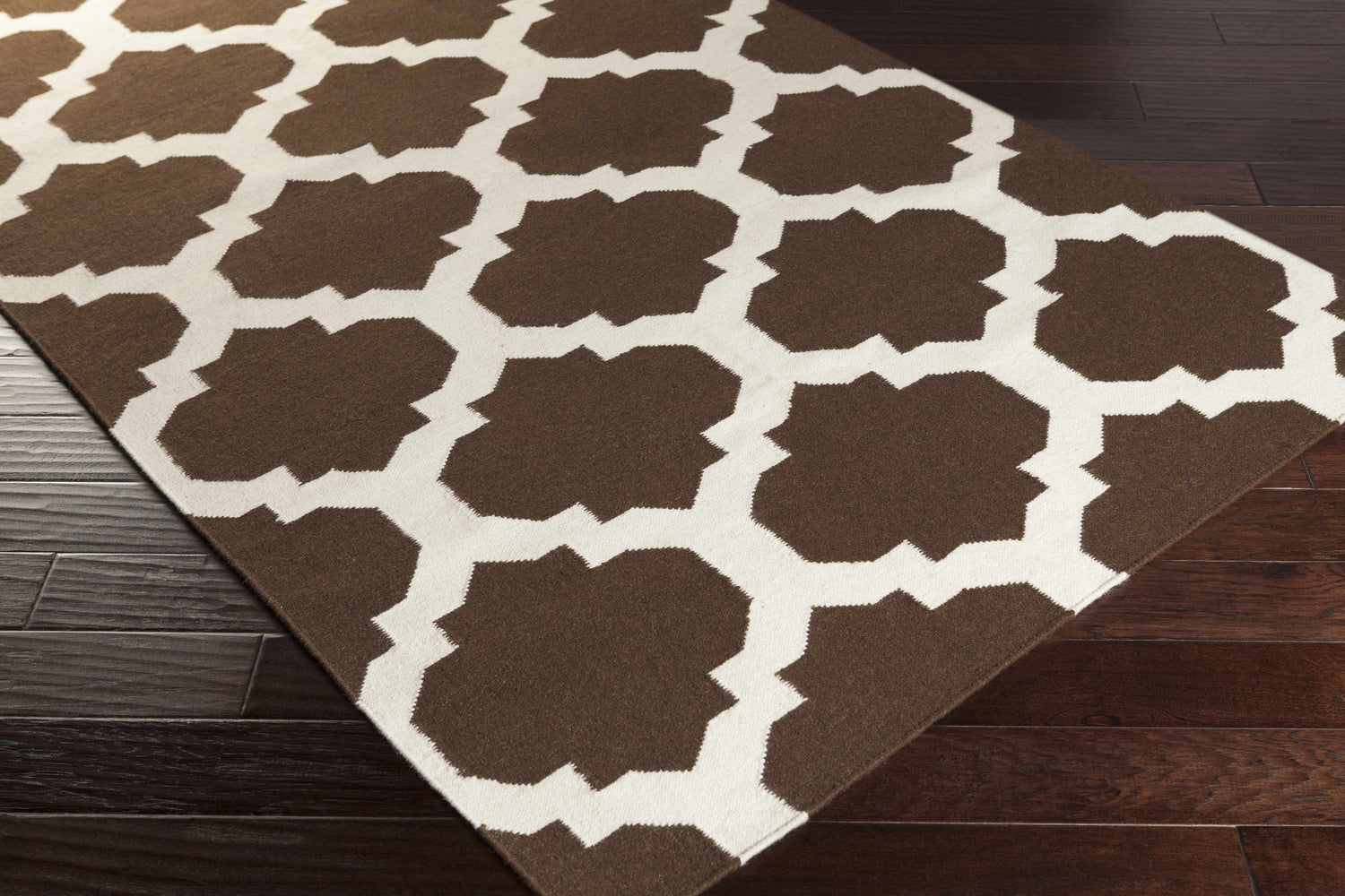 Close-up of the Depew Area Rug. The hand woven wool rug has a dark brown and ivory geometric pattern. Corner