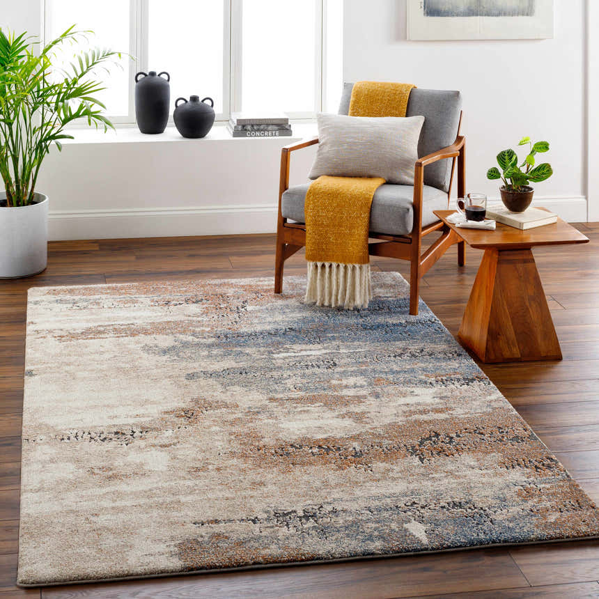 Living room scene with Deven Area Rug in camel, charcoal, and blue tones. Styled with a gray chair, wood side table, and potted plants. Roomscene-Rectangle