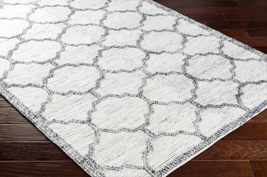 Close-up of the hand woven Dido Area Rug. Charcoal gray geometric pattern on a white base. Farmhouse style. Corner