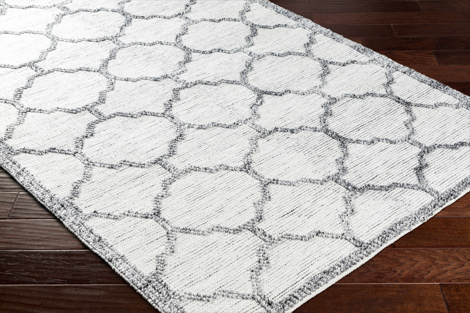 Close-up of the hand woven Dido Area Rug. Charcoal gray geometric pattern on a white base. Farmhouse style. Corner