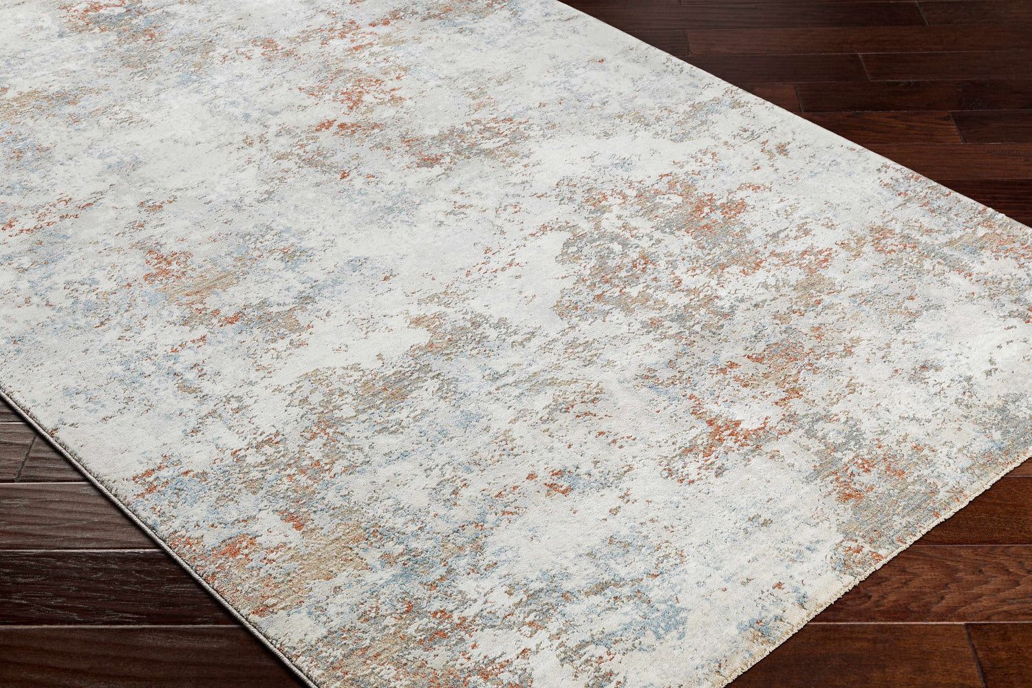 Close-up of the Dinos Thick Luxe Rug. Abstract pattern in gray, nutmeg, and light blue on a dark wood floor. Corner
