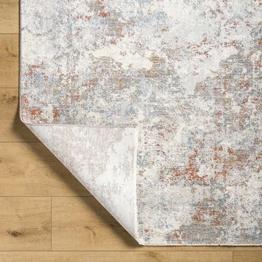 Close-up of the Dinos Thick Luxe Rug showing its abstract gray, blue, and nutmeg pattern and woven texture. Fold