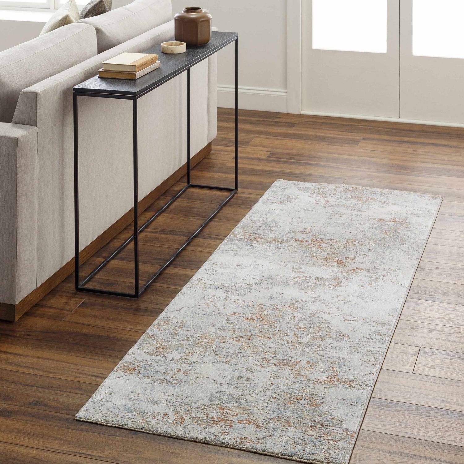 Living room scene with a Dinos Thick Luxe Rug in gray, brown, and nutmeg colors on hardwood floors. Modern sofa and console table. Roomscene-Runner
