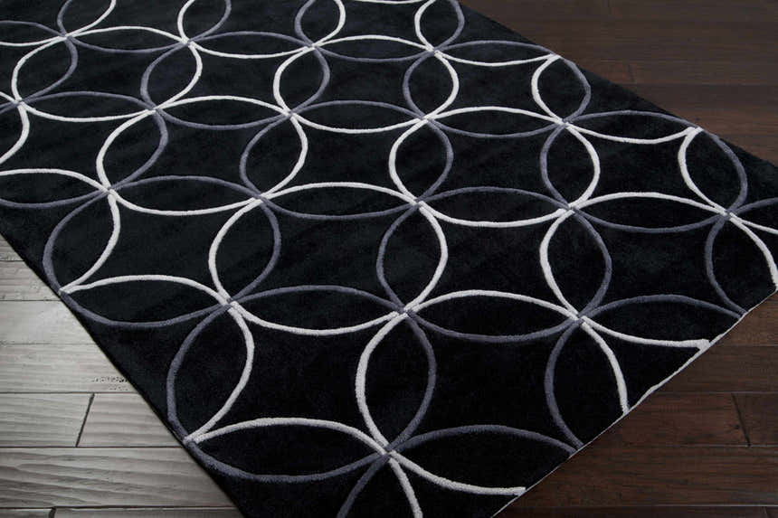 Close-up of the Delano Area Rug. Black rug with light gray and charcoal circle pattern on dark wood floor. Corner