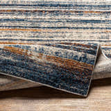 Close-up of the Dumaguil Thick Luxe Rug showing its blue, brown, and cream horizontal stripes and plush, textured weave. Fold