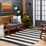Outdoor patio scene with a black and cream striped Douds Area Rug, wooden bench, and dark gray wall. Roomscene-Rectangle