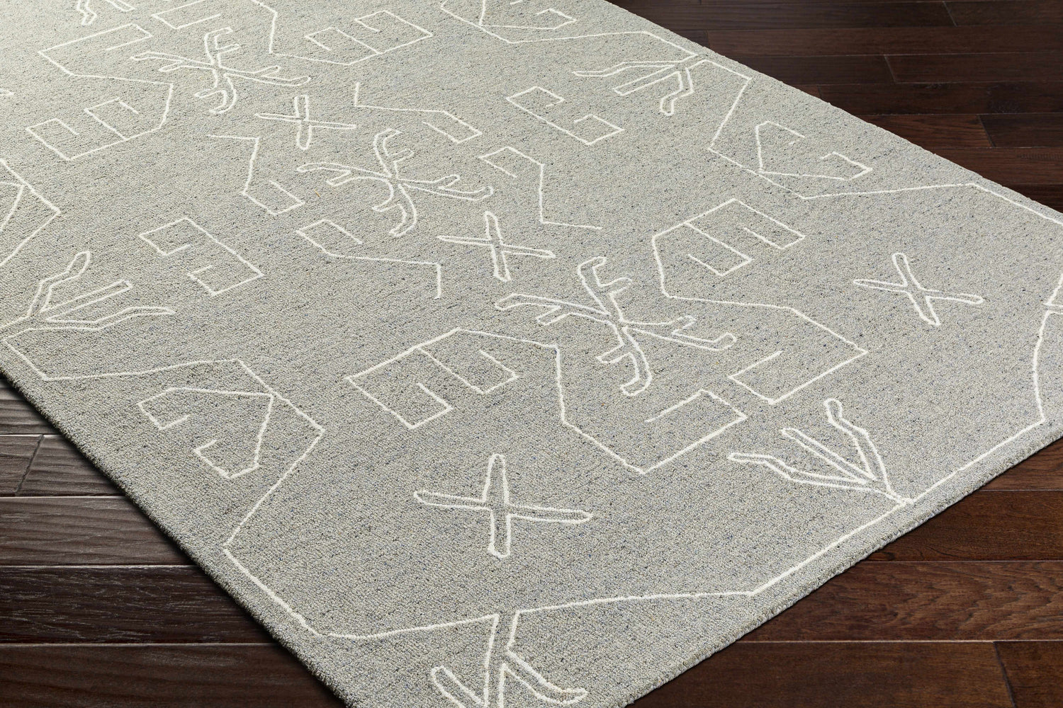 Close-up of the Duard Modern Wool Rug showing a gray rug with a white geometric pattern on dark wood flooring. Corner