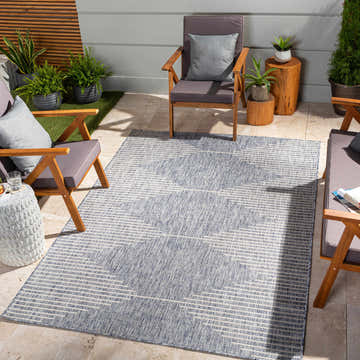 Outdoor patio scene with the Stephan Blue Outdoor Rug, wooden chairs, and potted plants. Roomscene-Rectangle