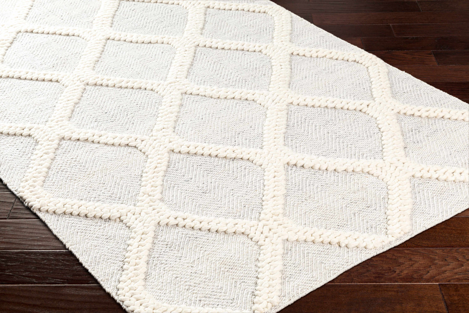Close-up of the Dusan Area Rug. Arctic Stone rug with a geometric trellis pattern on dark wood floors. Hand woven texture. Corner