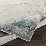 Close-up of the Devonport Thick Luxe Area Rug showing its light gray, taupe, and navy abstract pattern and texture. Fold