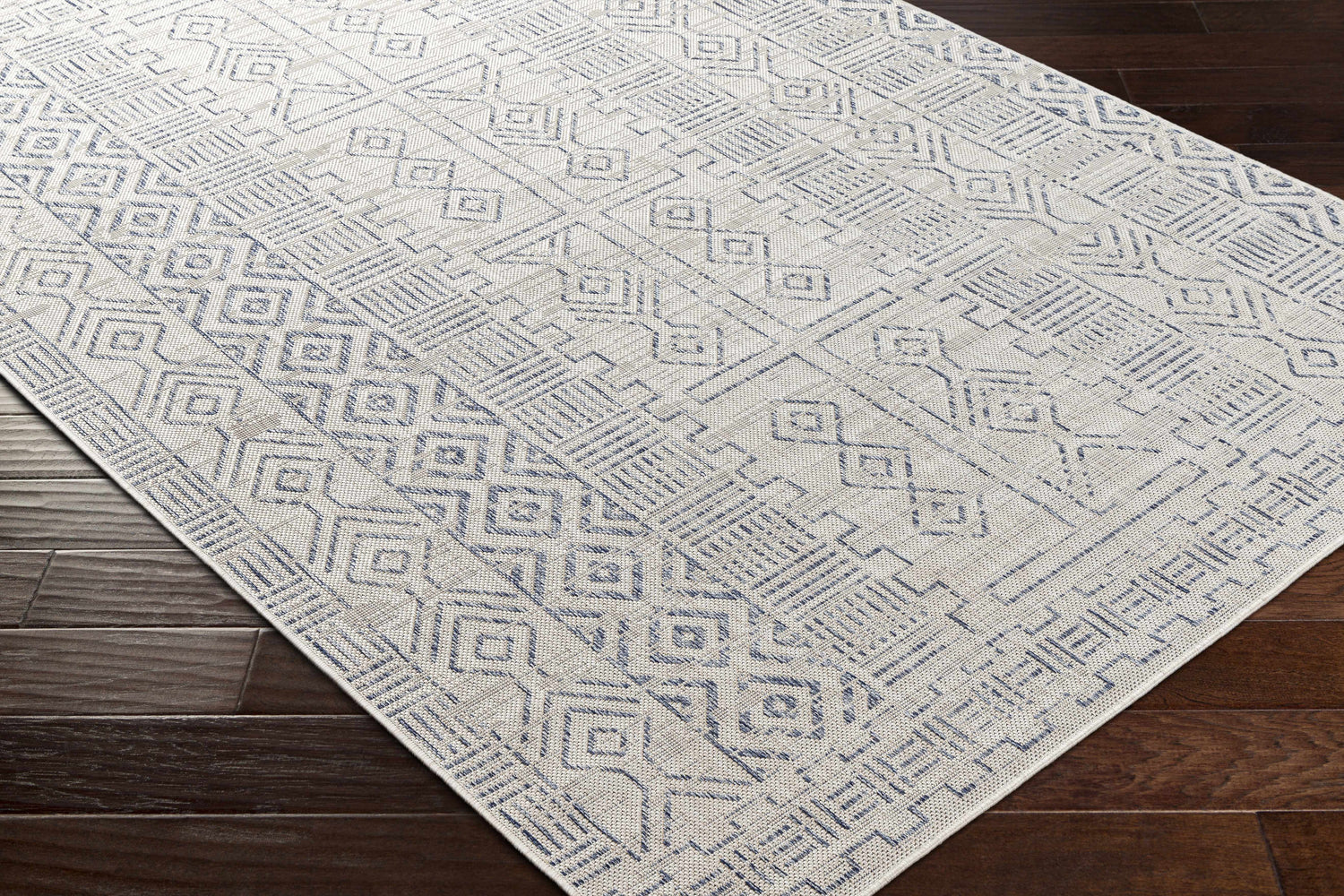 Close-up of the Epson Indoor & Outdoor Rug in oatmeal and blue, featuring a geometric, bohemian pattern on dark wood floors. Corner