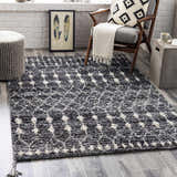 Living room scene with Erina Premium Rug in black, charcoal, and cream. Bohemian style with chair, ottoman, and gray wood floors. Roomscene-Rectangle