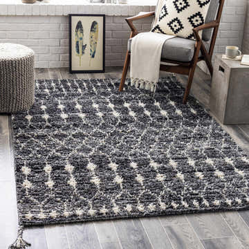 Living room scene with Erina Premium Rug in black, charcoal, and cream. Bohemian style with chair, ottoman, and gray wood floors. Roomscene-Rectangle