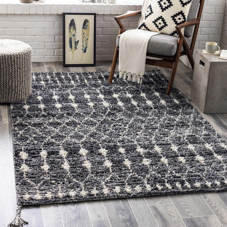 Living room scene with Erina Premium Rug in black, charcoal, and cream. Bohemian style with chair, ottoman, and gray wood floors. Roomscene-Rectangle