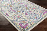 Close-up of the Errol Area Rug; a white rug with a traditional floral pattern in pink, blue, and yellow on dark wood floors. Corner