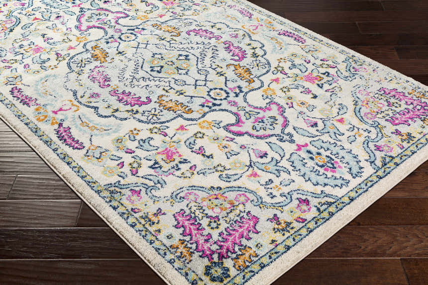 Close-up of the Errol Area Rug; a white rug with a traditional floral pattern in pink, blue, and yellow on dark wood floors. Corner