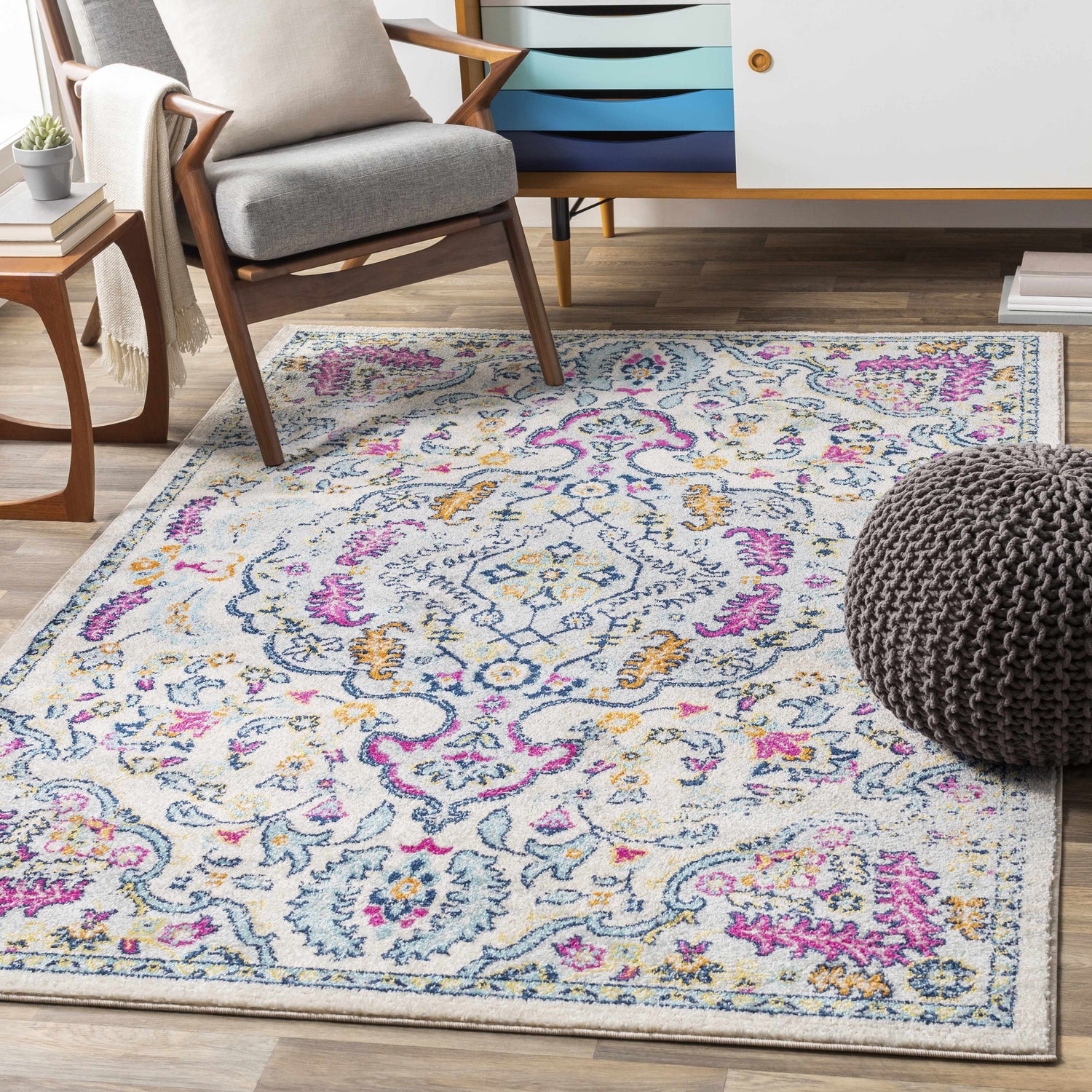 Living room scene with Errol Area Rug. Bohemian rug in aqua, pink, and yellow under gray chair and pouf. Roomscene-Rectangle