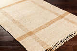 Close-up of Errin Jute Area Rug showing beige and camel geometric pattern, hand-woven texture, and fringe detail on dark wood floor. Corner