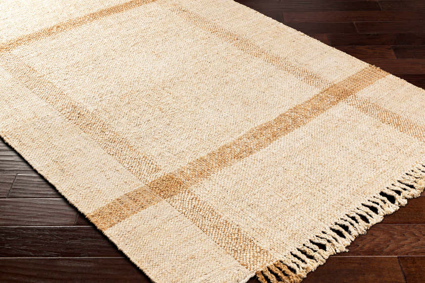 Close-up of Errin Jute Area Rug showing beige and camel geometric pattern, hand-woven texture, and fringe detail on dark wood floor. Corner