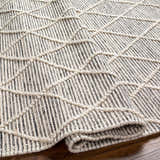 Close-up of Ezria Wool Rug with Tassels. Bone and dark gray rug with geometric pattern and hand-woven texture. Fold
