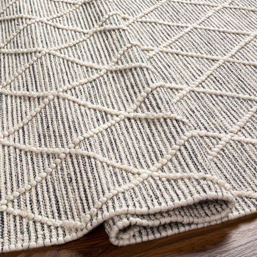 Close-up of Ezria Wool Rug with Tassels. Bone and dark gray rug with geometric pattern and hand-woven texture. Fold