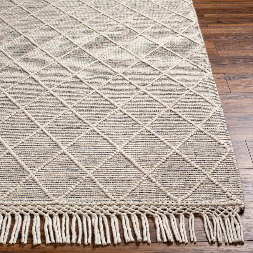 Close-up of Ezria Wool Rug with Tassels. Bone and dark gray rug with geometric diamond pattern and fringe. Front