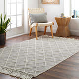 Living room scene with bone Ezria Wool Rug. Geometric rug with tassels, chair, and wood side table. Roomscene-Rectangle
