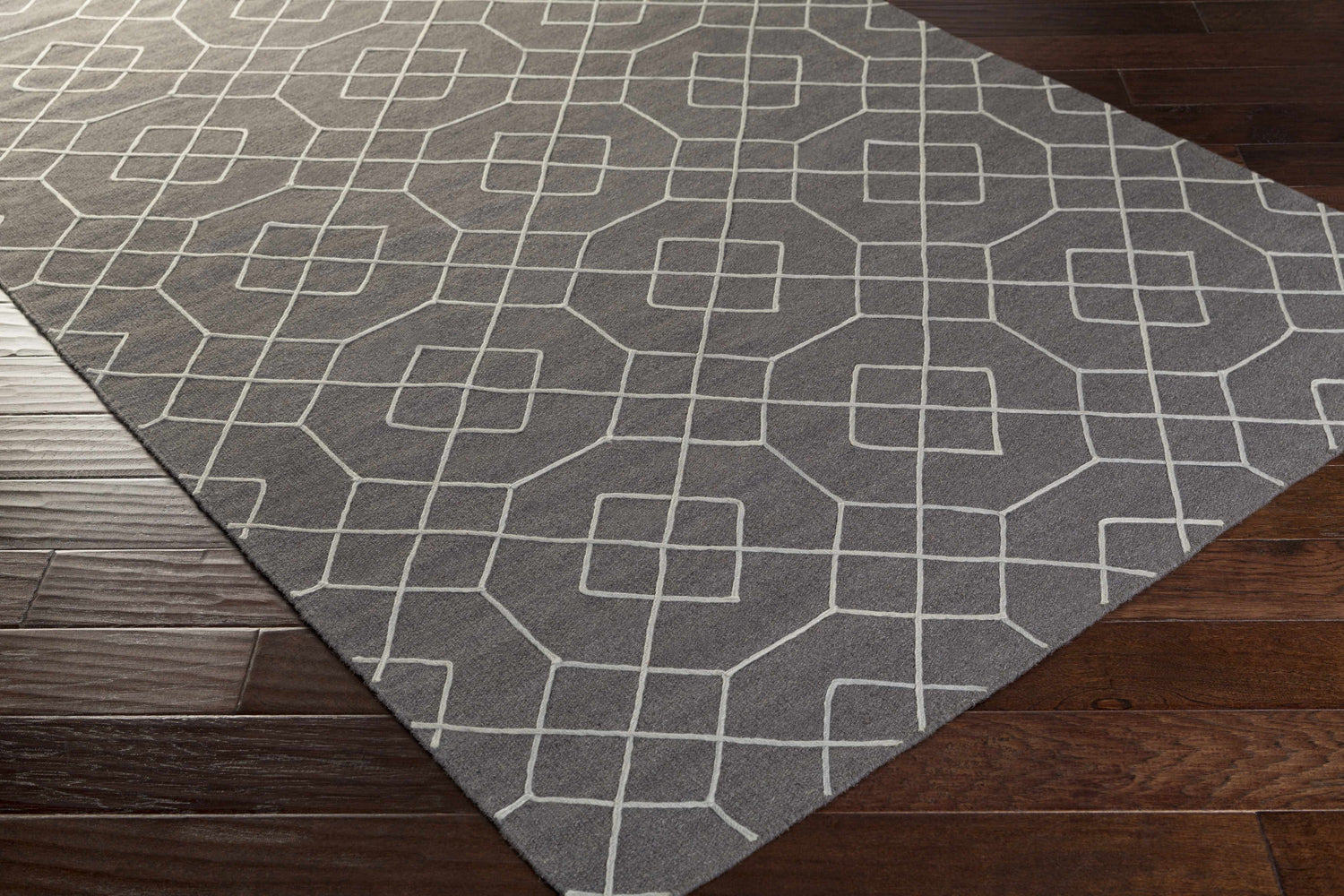 Close-up of Fareham Area Rug. Charcoal wool rug with ice blue geometric pattern on dark wood floor. Corner