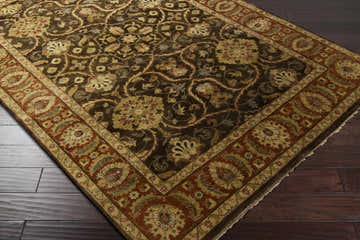 Close-up of the Fate Area Rug. Traditional floral pattern in burnt orange, brown, and blue on a dark brown 100% wool rug. Corner