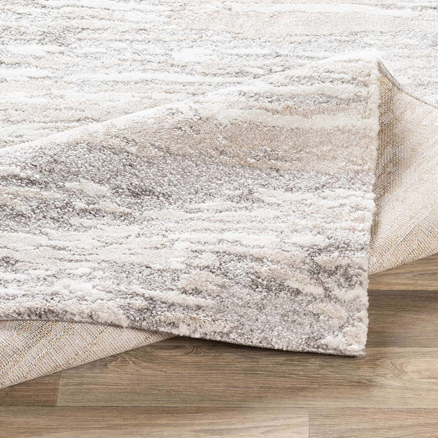 Close-up of the Ferrelview Area Rug showing a textured, abstract pattern in gray, ivory, and tan on a wood floor. Fold