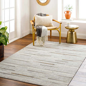 Bright room scene with a Fico Area Rug in dark brown, ivory, tan, and taupe. Features a chair, side table, and wood floors. Roomscene-Rectangle