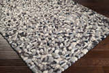 Close-up of a hand woven Fillmore Area Carpet. Wool rug features black, charcoal, cream, and gray pebble-like texture. Corner
