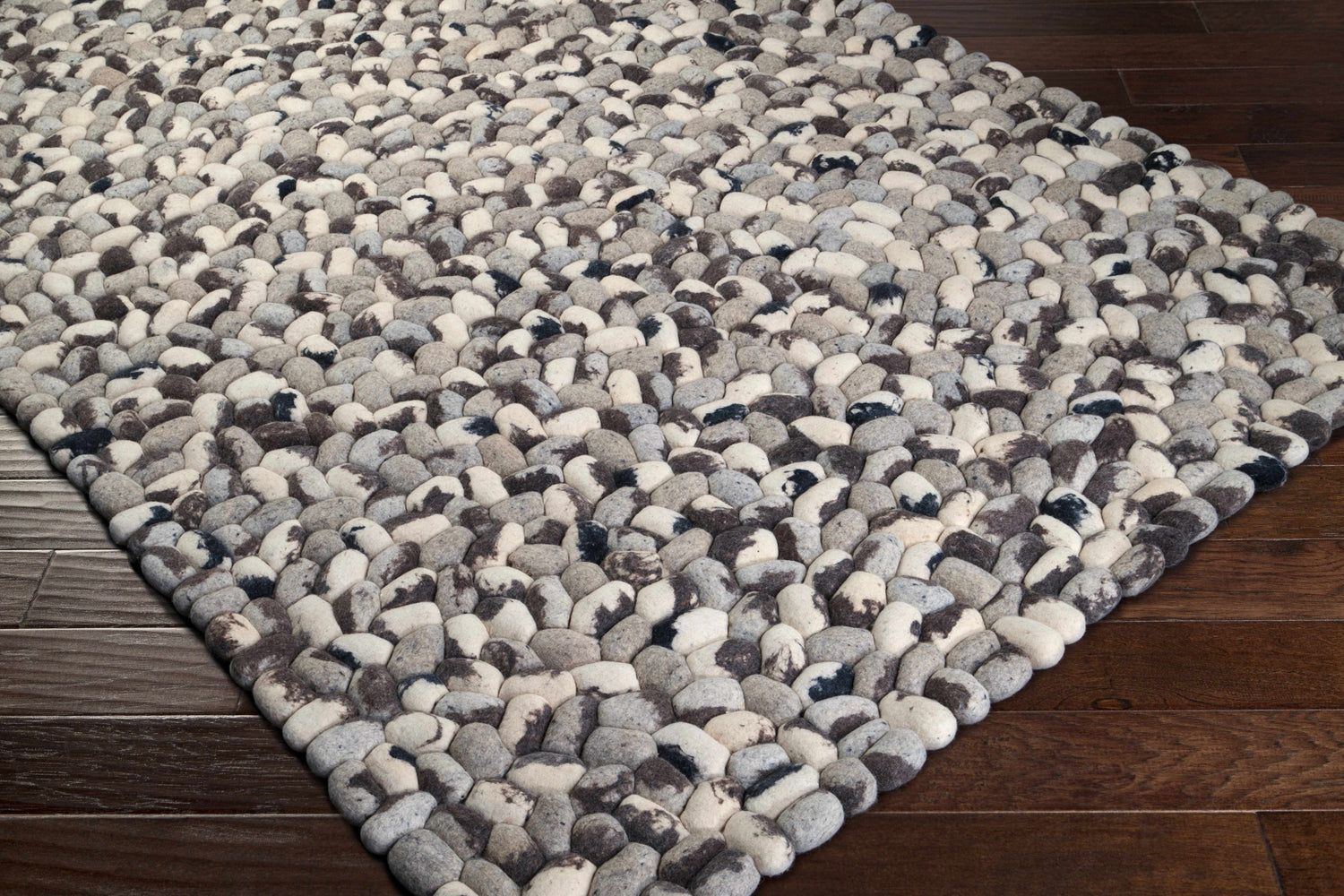Close-up of a hand woven Fillmore Area Carpet. Wool rug features black, charcoal, cream, and gray pebble-like texture. Corner