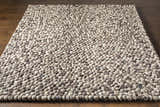 Close-up of the hand woven Fillmore Area Carpet. Wool rug with charcoal, cream, and gray pebble design. Contemporary style. Front