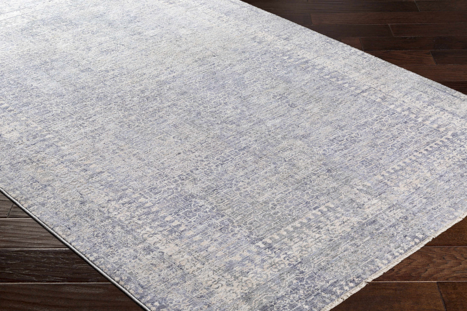 Close-up of the Foley Carved Statement Rug in blue, sage, and gray on a dark wood floor. Farmhouse style. Corner