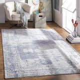 Living room scene with a blue Foley Carved Statement Rug, beige chair, concrete side table, and wood floors. Roomscene-Rectangle