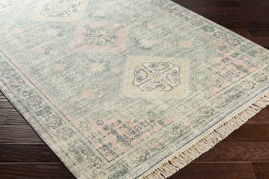 Close-up of the Foraker Sage Green Cotton Rug. Features a traditional design with sage, pink, and wheat hues. Hand-woven texture. Corner