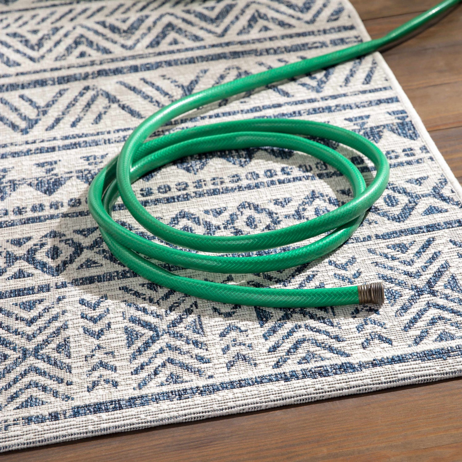 Close-up of the Novato Navy All Over Pattern Performance Rug with a blue and white geometric design and a green garden hose. Styleshot