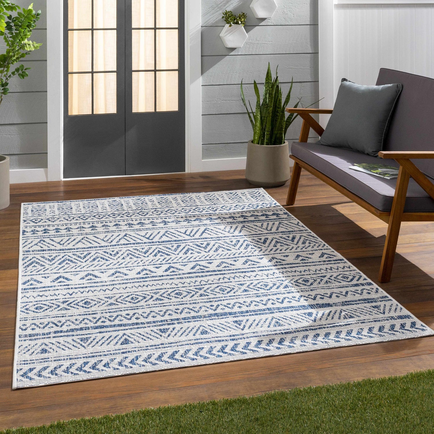 Outdoor patio scene with a blue and white Novato Navy All Over Pattern Performance Rug, gray loveseat, and potted plants. Roomscene-Rectangle