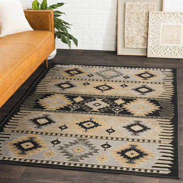Living room scene with a tan leather sofa and Foxburg Area Rug in charcoal, gray, light beige, and tan with a Southwestern pattern. Roomscene-Rectangle
