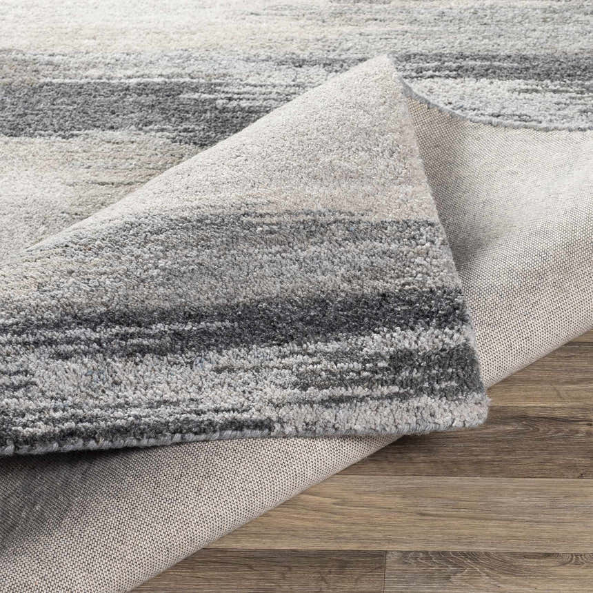 Close-up of the hand-tufted Farnhamville Area Carpet showing a gray and white striped pattern and wool texture. Fold