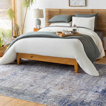 Bedroom scene with a Fairplains Washable Area Rug in charcoal, blue, and gray tones under a wooden bed frame. Roomscene-Rectangle