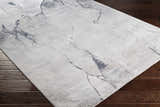 Close-up of the Gasquet Gray Marble Textured Luxe Rug showing charcoal and light gray marbled design on dark wood floor. Corner