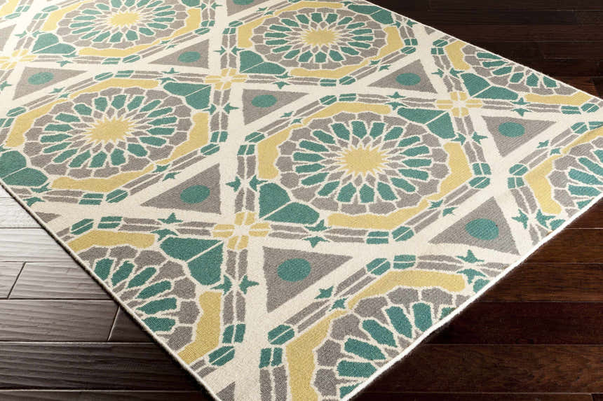 Close-up of Gaysville Area Carpet: ivory, light olive, teal, and olive geometric pattern on dark wood floor. Corner
